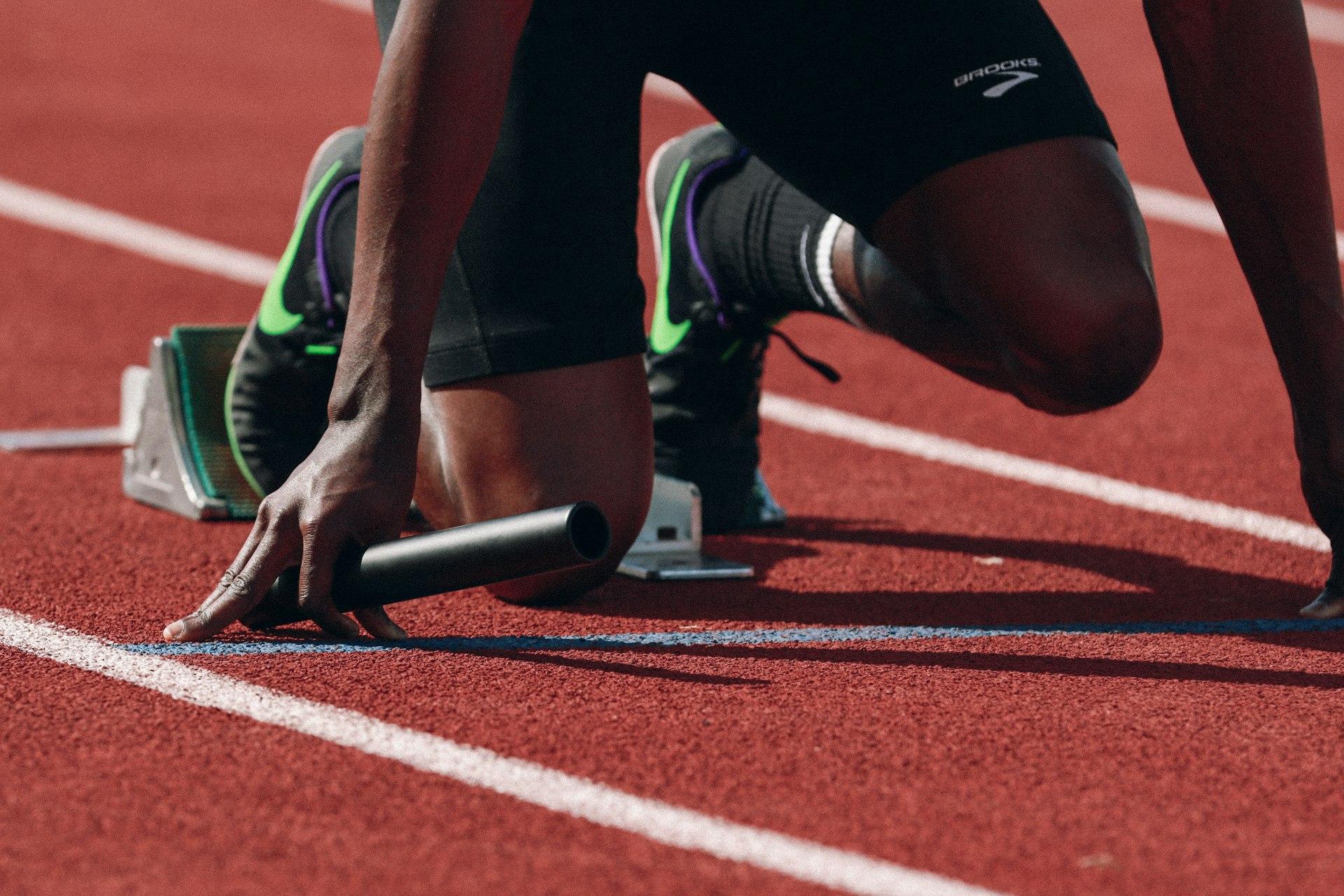 Athlete in the starting blocks on a running track, holding a relay baton